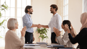 3 people clapping while two men in the middle shake hands
