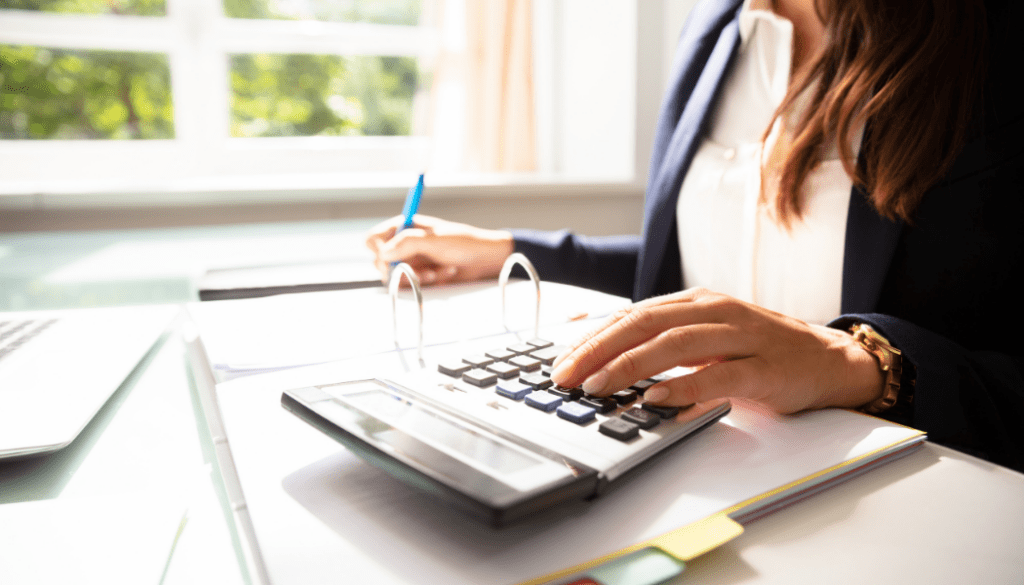 Woman sitting at a desk with an open binder while writing and typing on a calculator