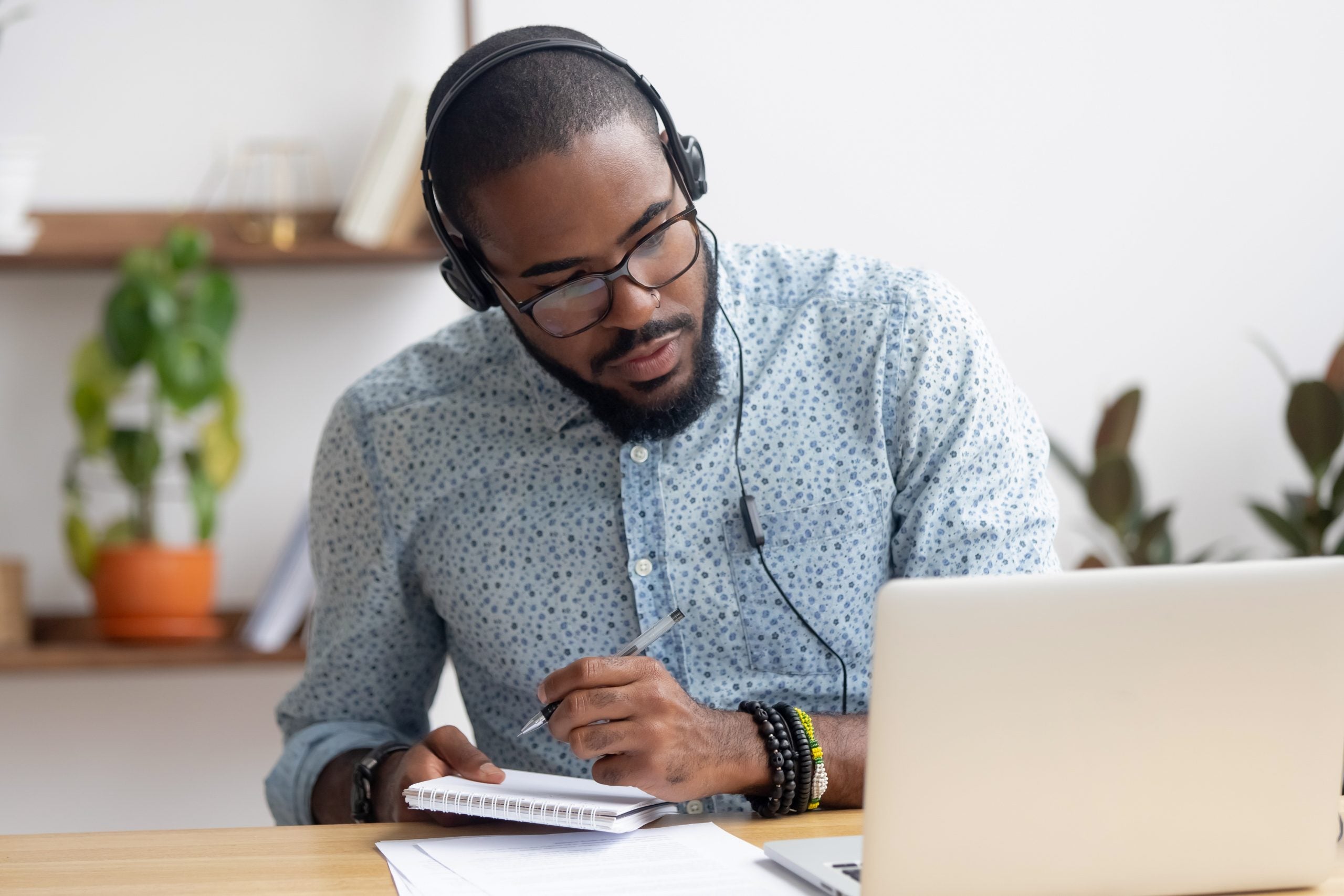 Focused,African,Business,Man,In,Headphones,Writing,Notes,In,Notebook