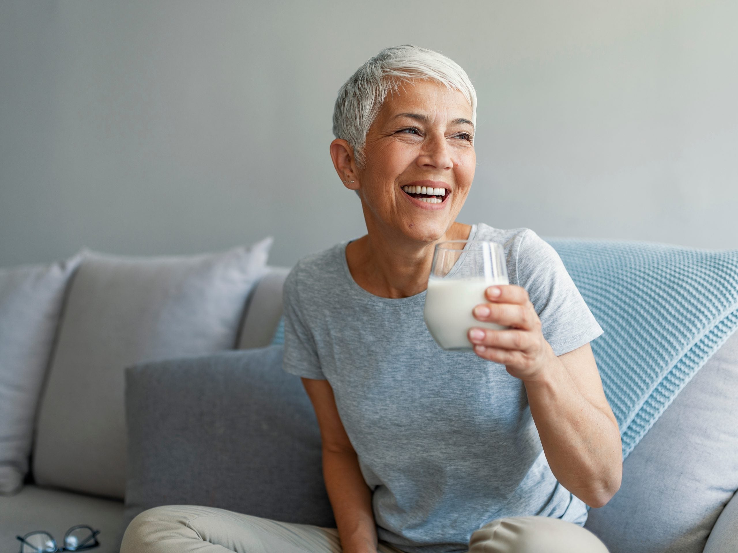 Senior woman's hands holding a glass of milk. Happy senior woman having fun while drinking milk at home. Senior Woman drinking a glass of milk to maintain her wellbeing.
