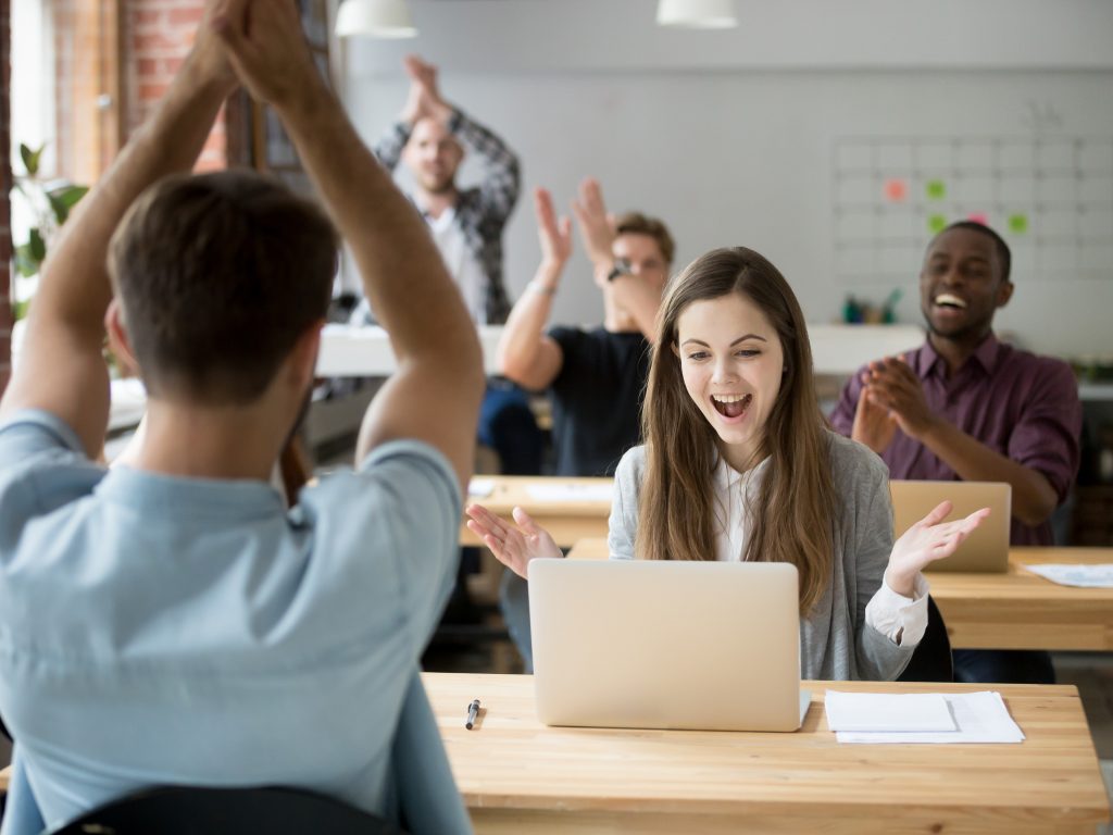 Excited woman looking at laptop screen surprised by good online news win achievement, corporate team colleagues congratulating coworker with business success clapping hands in coworking shared office