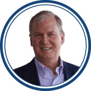 White circle with a dark blue outline features the headshot of a white man with gray hair wearing a navy blue blazer and purple collared shirt