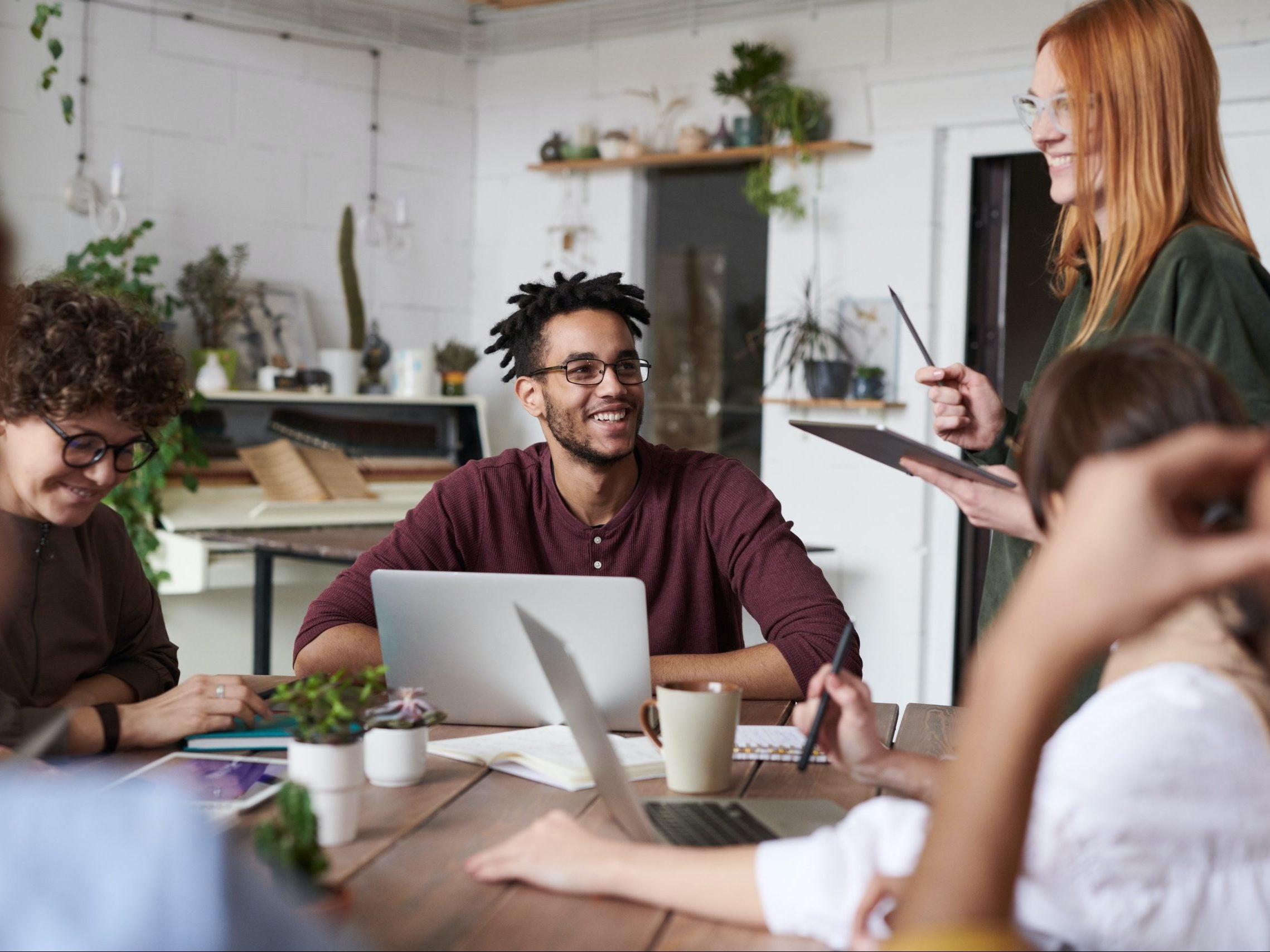 people sitting at a table with their attention directed to a woman with red hair as if she is presenting