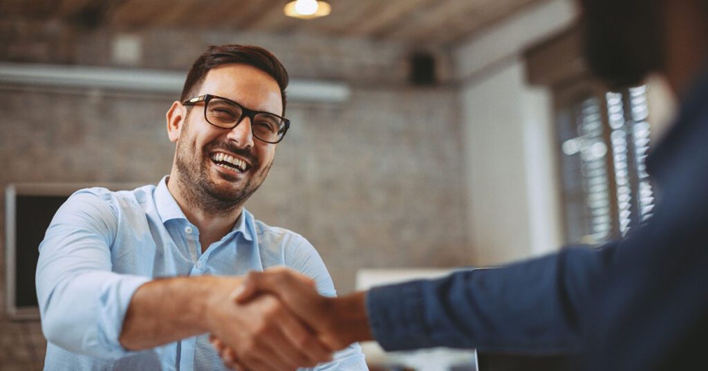 Young professional at work shaking coworkers hand and engaging in a conversation.