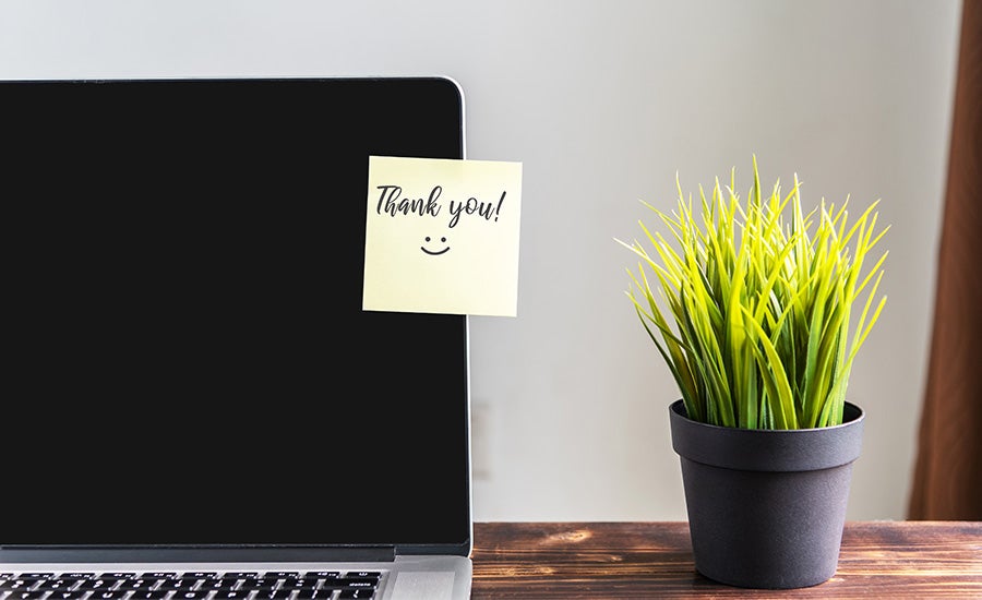 Thank you sticky note on a laptop with a desk plant next to the laptop