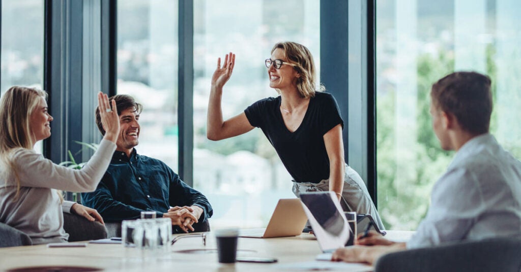 Young employees high fiving around a table