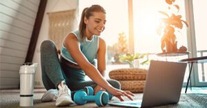 Young woman sitting on floor at home with laptop, about to exercise