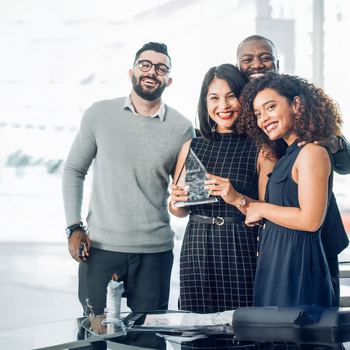 Someone off camera is taking a picture of five employees, one of which is holding a glass award in the center of the group.