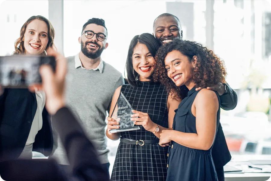 Someone off camera is taking a picture of five employees, one of which is holding a glass award in the center of the group.
