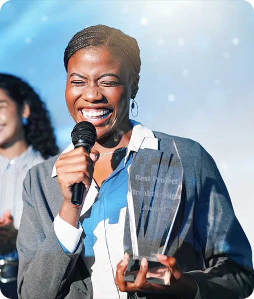 A woman with braids in a business outfit is smiling while holding an award and a microphone. 
